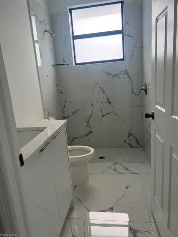 Bathroom with tile flooring, tiled shower, toilet, and vanity