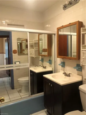 Full bathroom with shower / bath combination with glass door, vanity, toilet, and tile walls.