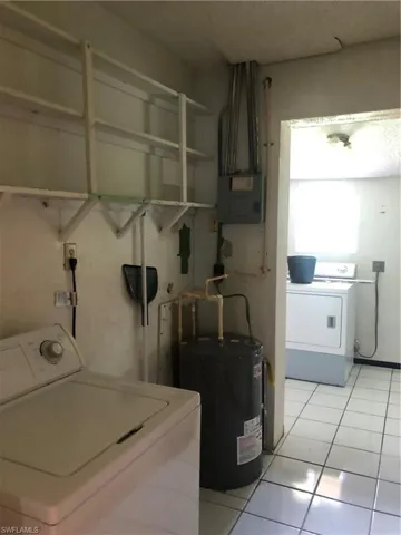 Washroom featuring light tile patterned floors, electric panel, independent washer and dryer, and water heater