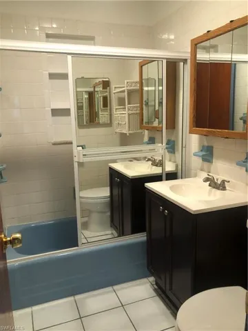 Full bathroom featuring shower / bath combination with glass door, vanity, tile walls, toilet, and tile patterned floors