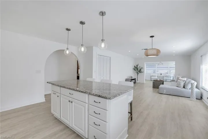 Open plan kitchen featuring light vinyl wood-style floors, white cabinetry, granite countertops, a center island, and decorative light fixtures.