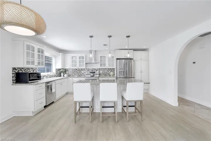 Kitchen featuring white cabinets, a kitchen island, stainless steel appliances, light wood-type flooring, and wall chimney range hood.