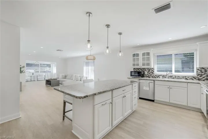 Open floor plan with light and bright kitchen, hanging light fixtures, stainless appliances, and white cabinets. New vinyl wood-look floors.