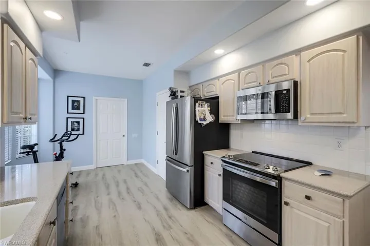 Kitchen featuring decorative backsplash, light brown cabinetry, light wood-type flooring, and stainless steel appliances
