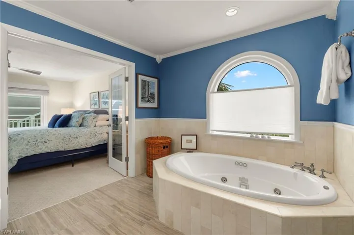 Ensuite bathroom with wood finished floors, a tub with jets, wainscoting, and crown molding