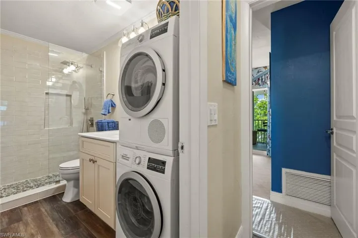 Washroom featuring stacked washing machine and dryer, crown molding, and dark wood finished floors