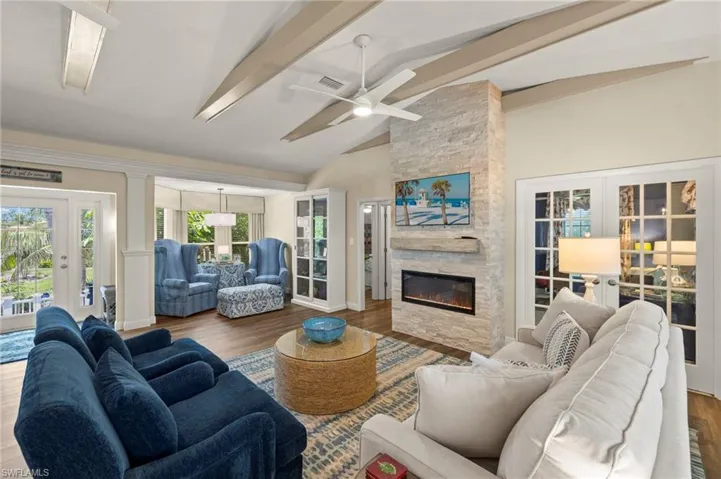 Living area featuring french doors, beamed ceiling, ceiling fan, a fireplace, and wood finished floors