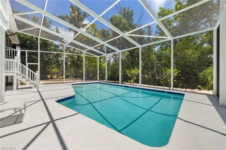 Outdoor pool featuring a patio area, stairs, view of scattered trees, and glass enclosure
