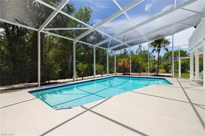 Swimming pool featuring a patio, glass enclosure, and view of scattered trees