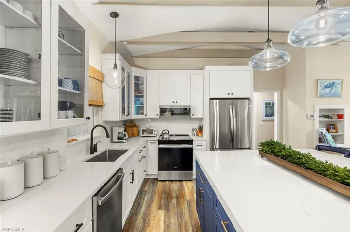 Kitchen with stainless steel appliances, blue cabinets, dark wood-type flooring, white cabinets, and light stone countertops