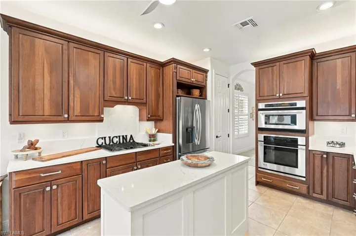 Kitchen featuring wood-finish cabinetry, white solid-surface countertops, a center island with solid-surface counter, and integrated stainless steel appliances