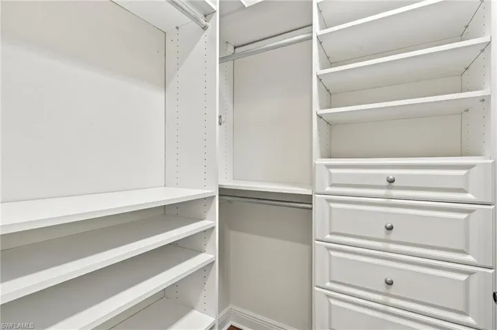 Custom closet system featuring multiple hanging rods, adjustable shelving, and integrated drawers with panel detailing and polished hardware