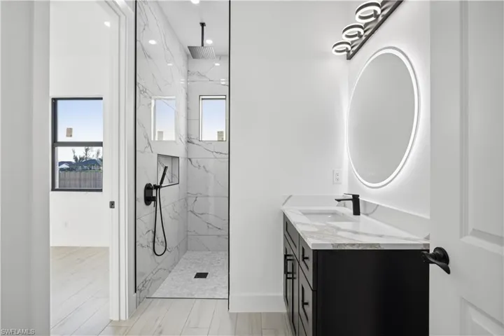 Bathroom featuring tiled shower, vanity, tile patterned floors, and plenty of natural light