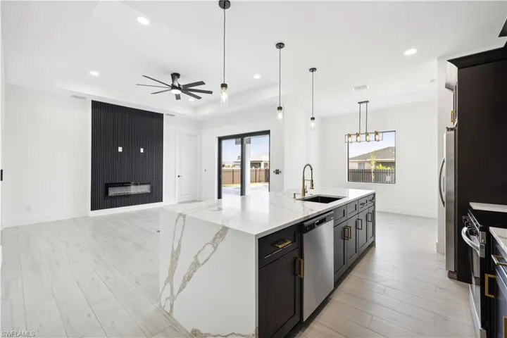 Kitchen with a tray ceiling, sink, light hardwood / wood-style floors, appliances with stainless steel finishes, and a kitchen island with sink