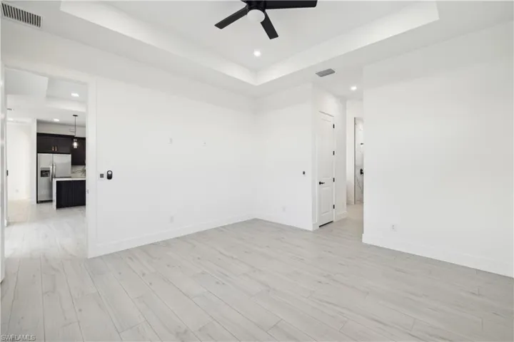Empty room with light wood-type flooring, ceiling fan, and a raised ceiling
