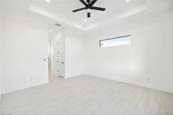 Unfurnished room with ceiling fan, light wood-type flooring, and a tray ceiling