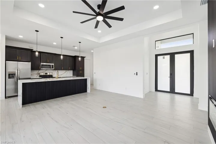 Kitchen featuring stainless steel appliances, french doors, a raised ceiling, and a center island with sink