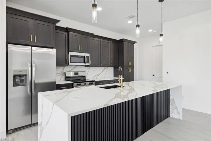 Kitchen with sink, light stone countertops, a center island with sink, appliances with stainless steel finishes, and backsplash