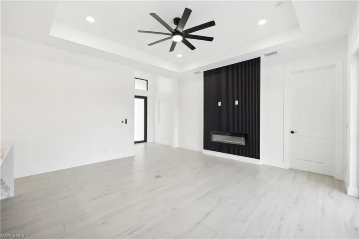 Unfurnished living room featuring light hardwood / wood-style floors, a fireplace, ceiling fan, and a tray ceiling