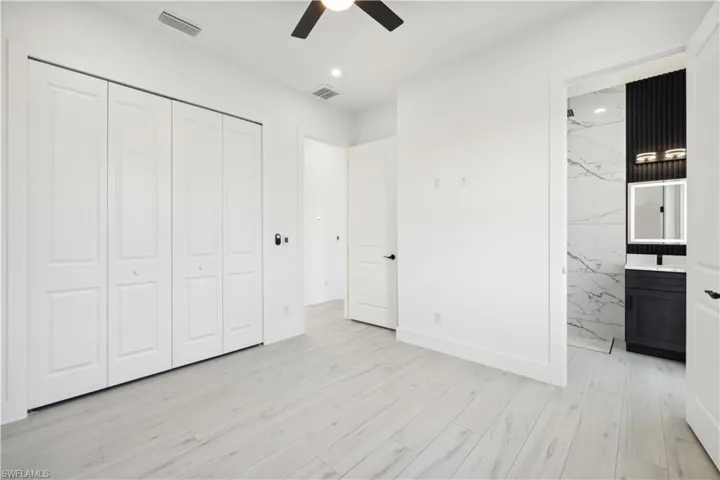 Unfurnished bedroom featuring a closet, ensuite bath, ceiling fan, and light wood-type flooring