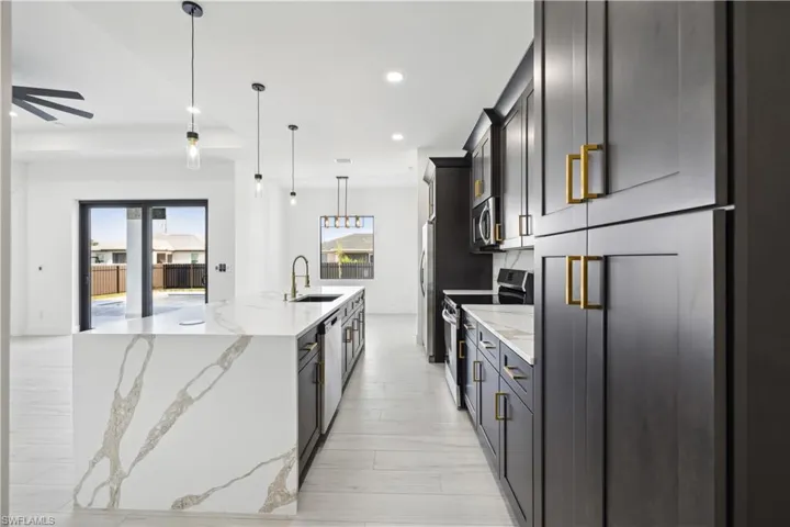 Kitchen featuring light stone counters, a kitchen island with sink, light hardwood / wood-style floors, hanging light fixtures, and appliances with stainless steel finishes