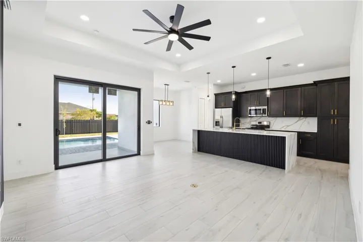 Kitchen featuring appliances with stainless steel finishes, a tray ceiling, hanging light fixtures, a kitchen island with sink, and ceiling fan