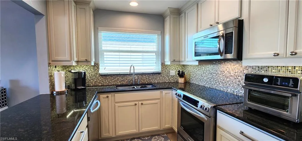 Kitchen with appliances with stainless steel finishes, tasteful backsplash, sink, dark stone countertops, and white cabinetry