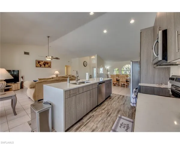 Kitchen with stainless steel appliances, a kitchen island with sink, ceiling fan, sink, and lofted ceiling