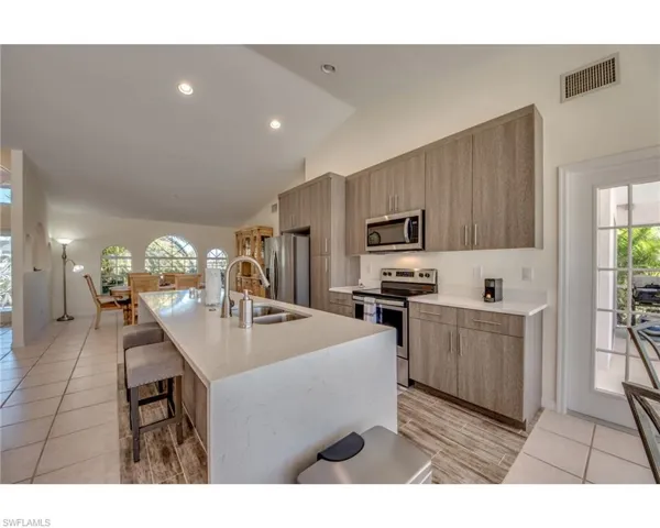 Kitchen with sink, stainless steel appliances, an island with sink, vaulted ceiling, and light tile patterned flooring