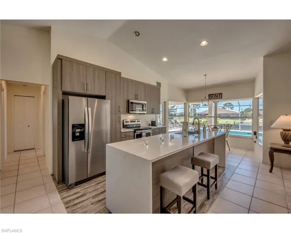 Kitchen featuring hanging light fixtures, stainless steel appliances, vaulted ceiling, a kitchen island with sink, and light tile patterned floors