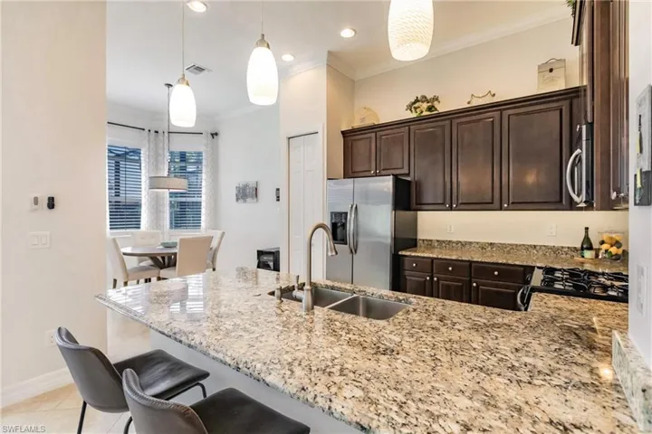 Kitchen with decorative light fixtures, a kitchen bar, dark brown cabinets, appliances with stainless steel finishes, and light tile floors
