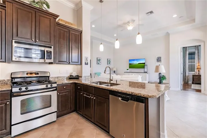 Kitchen featuring kitchen peninsula, stainless steel appliances, light tile floors, hanging light fixtures, and sink