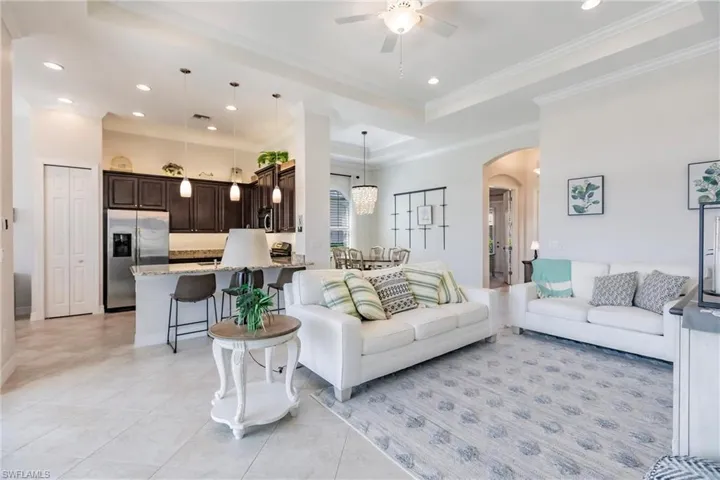 Living room featuring crown molding, light tile flooring, ceiling fan, and a raised ceiling