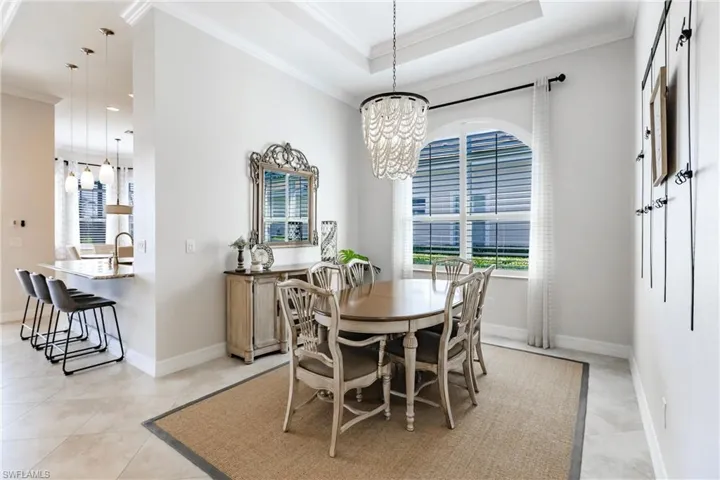 Tiled dining area with crown molding, sink, a raised ceiling, and an inviting chandelier
