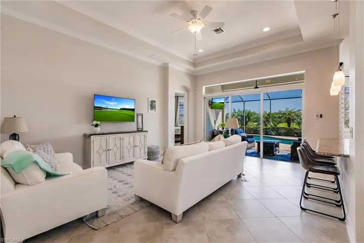 Tiled living room with ornamental molding, ceiling fan, and a tray ceiling