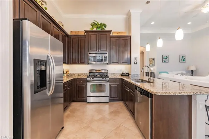 Kitchen with kitchen peninsula, stainless steel appliances, pendant lighting, light tile floors, and sink