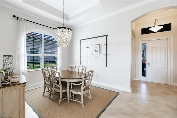 Dining area with a raised ceiling, an inviting chandelier, crown molding, and light tile flooring
