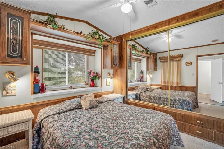 Carpeted bedroom featuring lofted ceiling, a textured ceiling, multiple windows, and ceiling fan