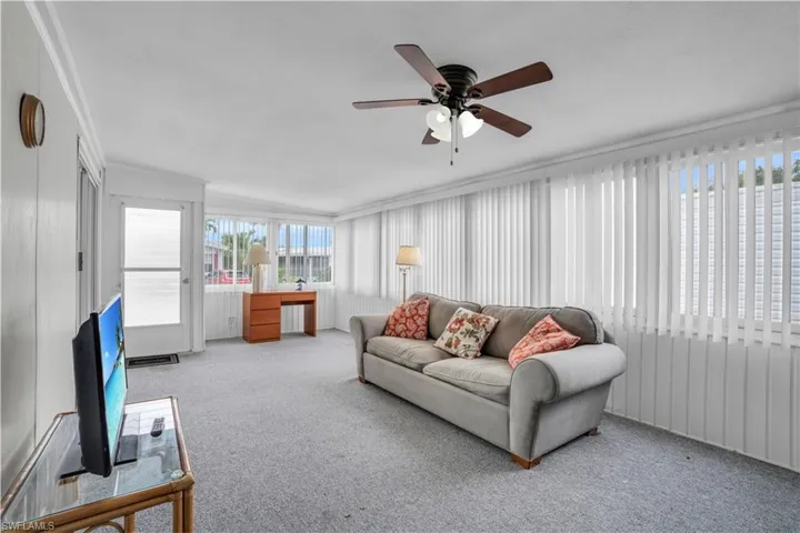 Living room featuring ceiling fan, a wealth of natural light, carpet flooring, and crown molding