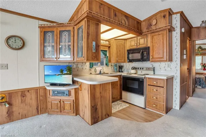 Kitchen featuring white range with electric cooktop, a textured ceiling, kitchen peninsula, and light carpet
