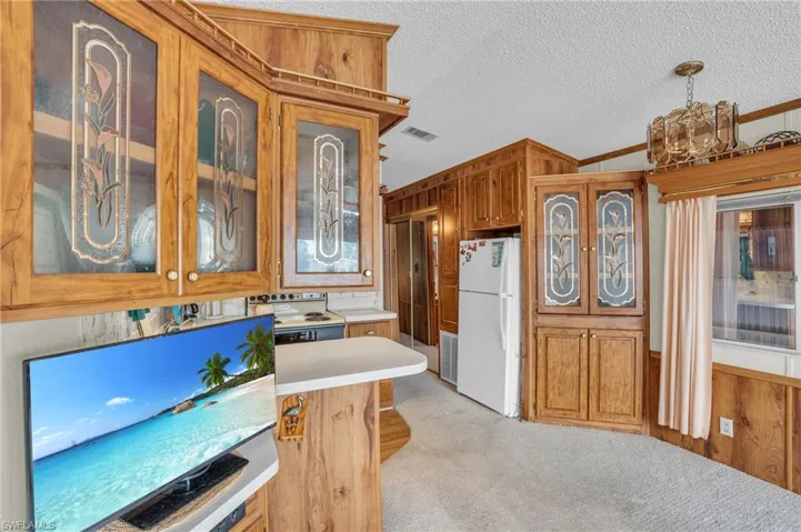 Kitchen with a textured ceiling, crown molding, pendant lighting, light carpet, and white appliances