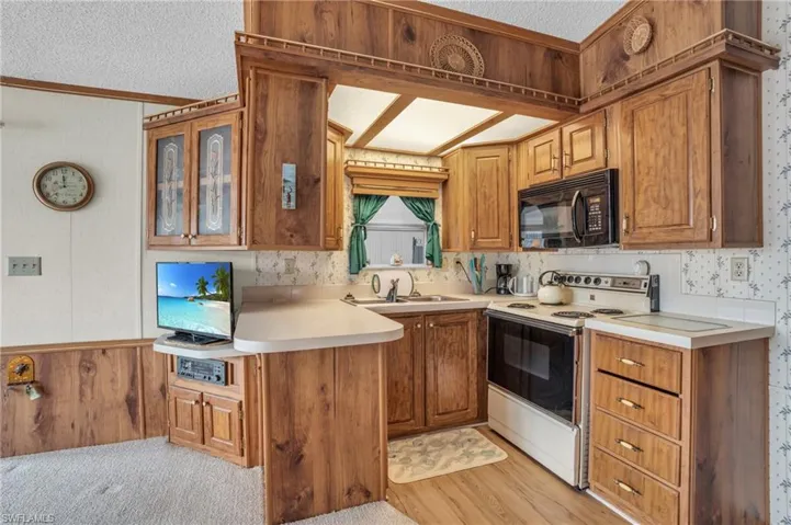 Kitchen with a textured ceiling, light carpet, electric stove, beam ceiling, and sink