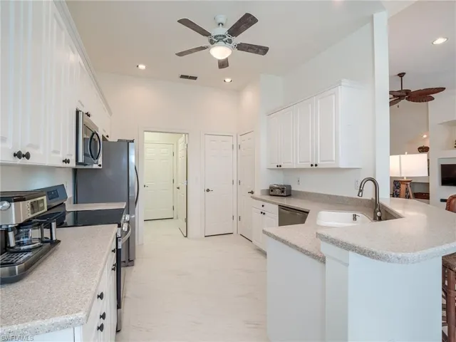 Kitchen featuring kitchen peninsula, white cabinets, ceiling fan, appliances with stainless steel finishes, and sink