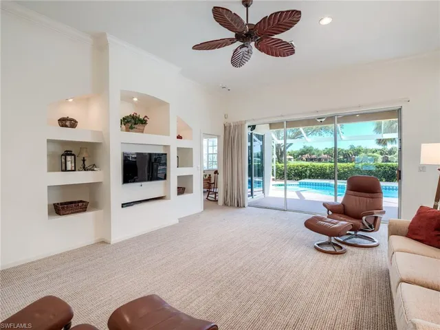 Living room featuring built in shelves, light colored carpet, ornamental molding, and ceiling fan