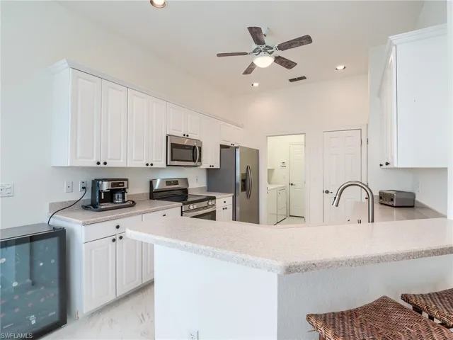 Kitchen featuring kitchen peninsula, beverage cooler, washer and dryer, appliances with stainless steel finishes, and a kitchen bar