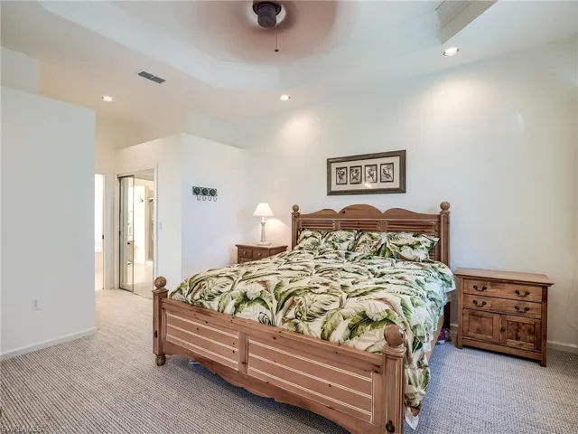Carpeted bedroom with ceiling fan, connected bathroom, and a tray ceiling