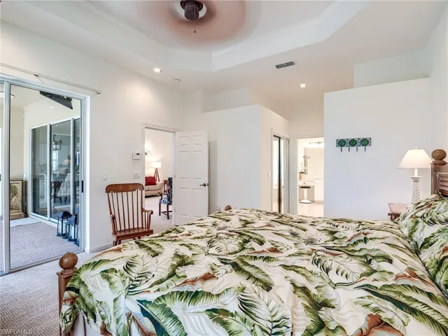 Carpeted bedroom with ceiling fan, a tray ceiling, crown molding, ensuite bathroom, and access to exterior
