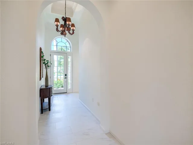 Hallway with a high ceiling, a notable chandelier, and white tile floors