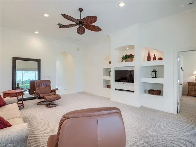 Living room featuring built in shelves, light carpet, ornamental molding, and ceiling fan