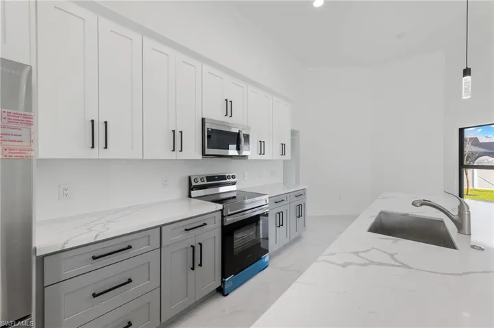 Two tone kitchen with stainless steel appliances, two tone color scheme, light stone counters, ornamental molding, and decorative light fixtures